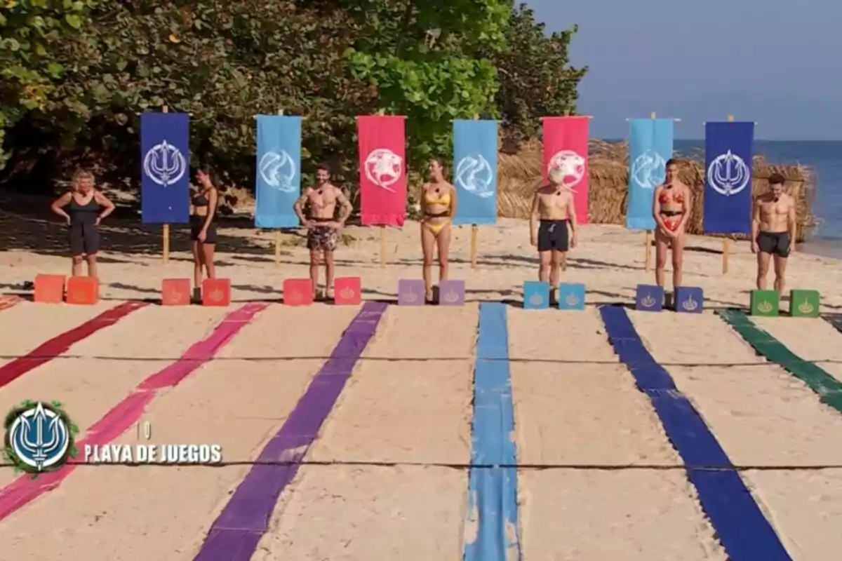 Un grup de persones a la platja drets davant de camins de colors i banderes, preparats per a una competició. Un grup de persones a la platja drets davant de camins de colors i banderes, preparats per a una competició.