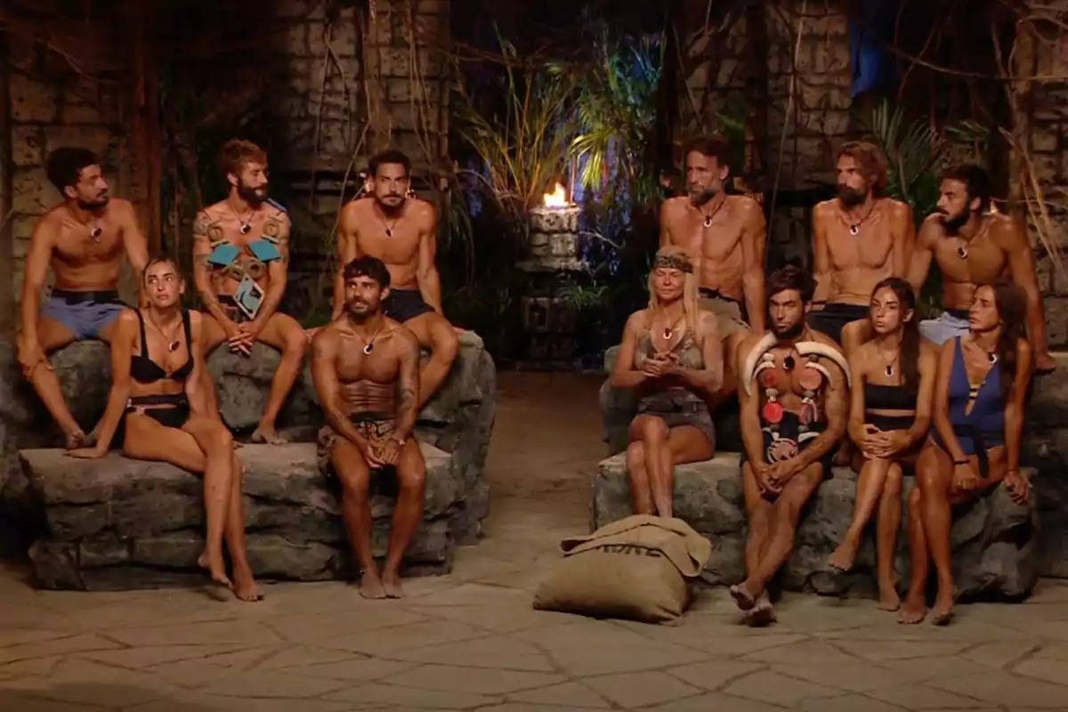 Un grup de persones assegudes en un entorn d'estil tribal amb una torxa encesa al fons. Captura de 'Supervivientes'.