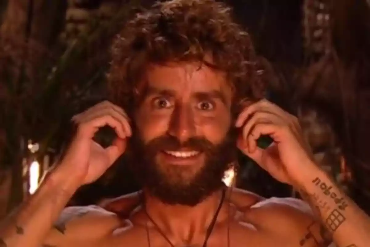 Pelayo Díaz smiles while touching his ears with both hands in an outdoor setting lit by fire. Screenshot from 'Supervivientes' Pelayo Díaz smiles while touching his ears with both hands in an outdoor setting lit by fire. Screenshot from 'Supervivientes'