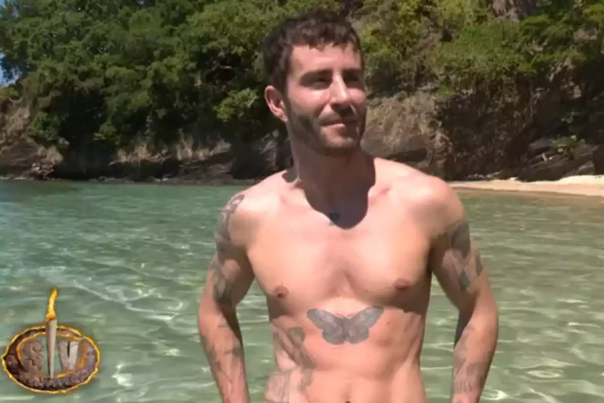 Pelayo Díaz amb tatuatges al tors està dret a l'aigua clara d'una platja amb vegetació al fons. Captura de 'Supervivientes'. Pelayo Díaz amb tatuatges al tors està dret a l'aigua clara d'una platja amb vegetació al fons. Captura de 'Supervivientes'.