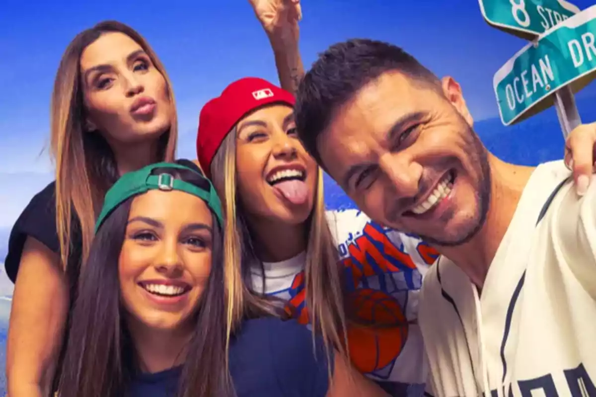 Un grupo de cuatro personas sonríe y posa para una selfie, con gorras y ropa casual, frente a un fondo azul con señales de tráfico.