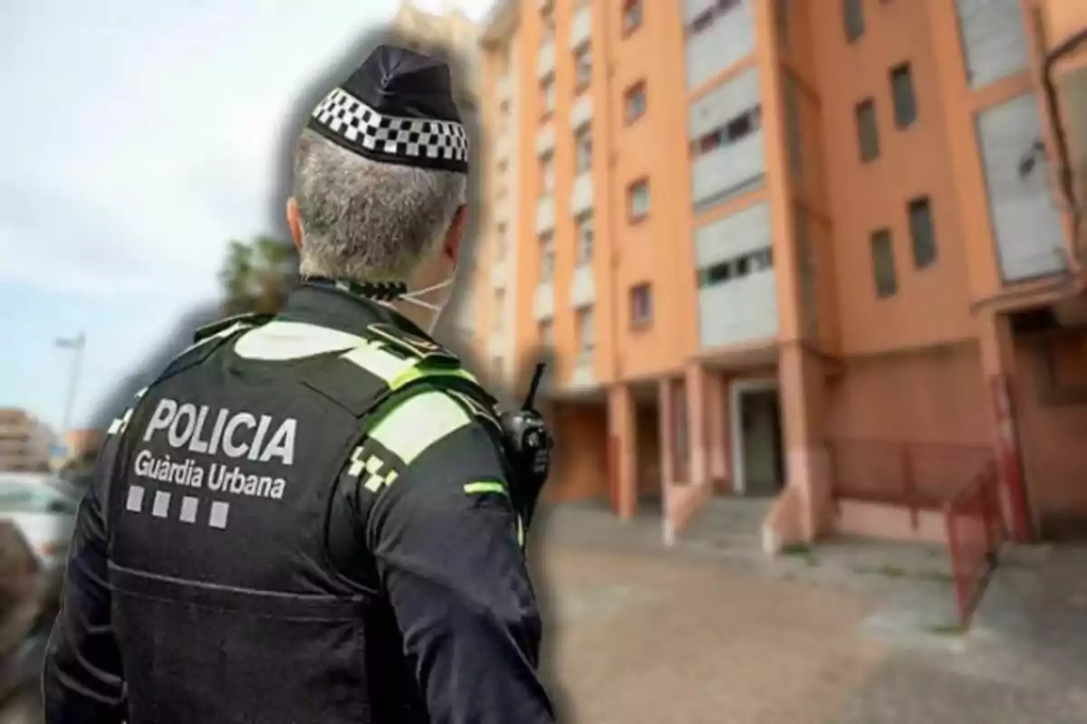 Un agent de la policia urbana d'esquena observa un edifici residencial.