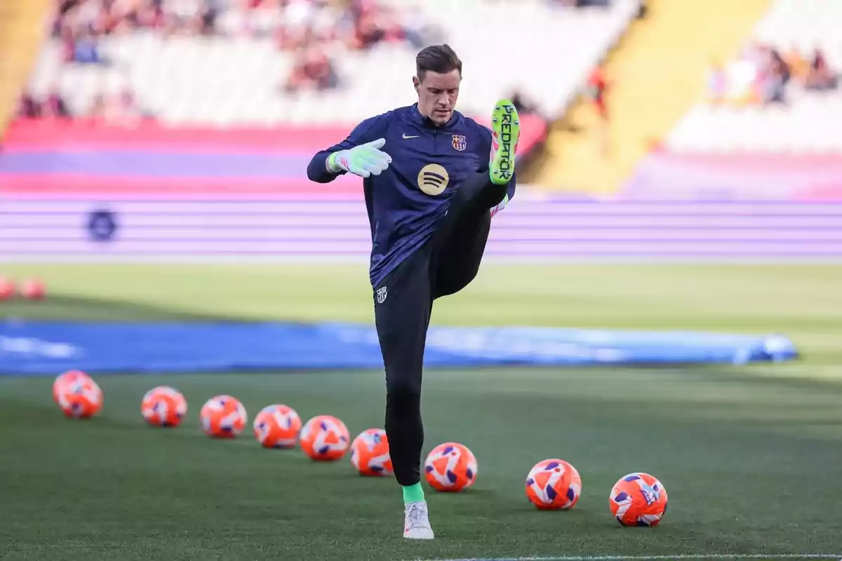 Un jugador de futbol fa exercicis d'escalfament al camp amb diverses pilotes taronges al voltant. Un jugador de futbol fa exercicis d'escalfament al camp amb diverses pilotes taronges al voltant.