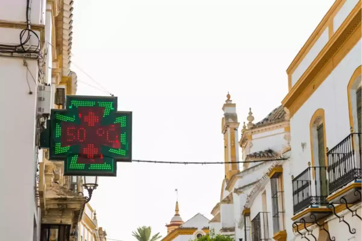 Un rètol de farmàcia mostra una temperatura de 50 graus Celsius en un carrer amb edificis tradicionals.