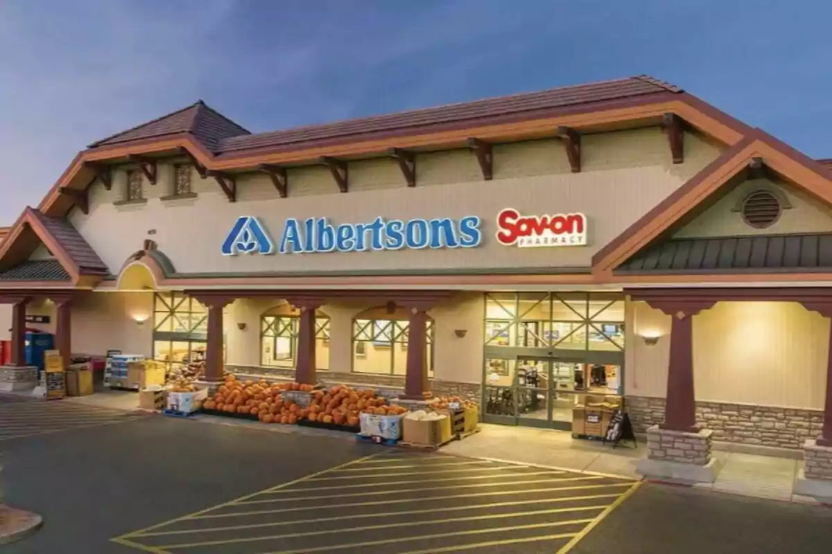 La imatge mostra la façana d'una botiga Albertsons amb un rètol de Savon Pharmacy, hi ha carabasses i productes a l'entrada i el cel està clar.