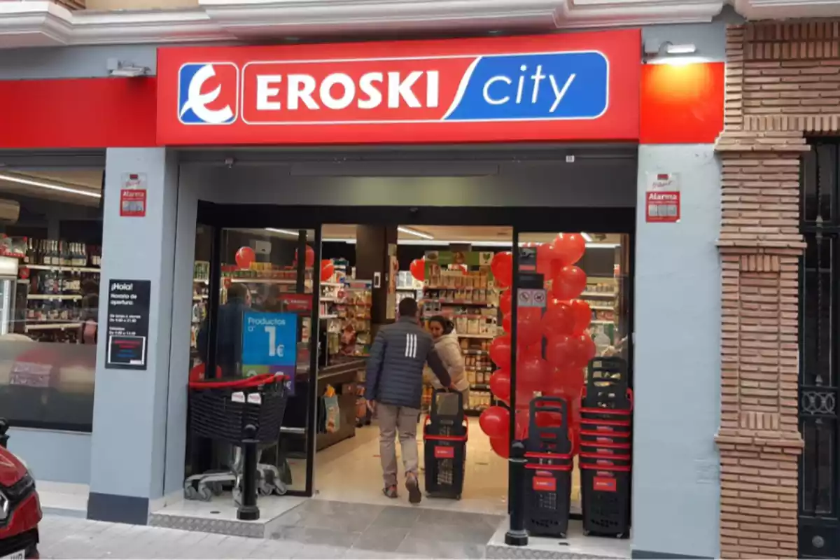 Exterior d'un supermercat d'Eroski i un client entrant per la porta de la botiga amb un carretó a la mà
