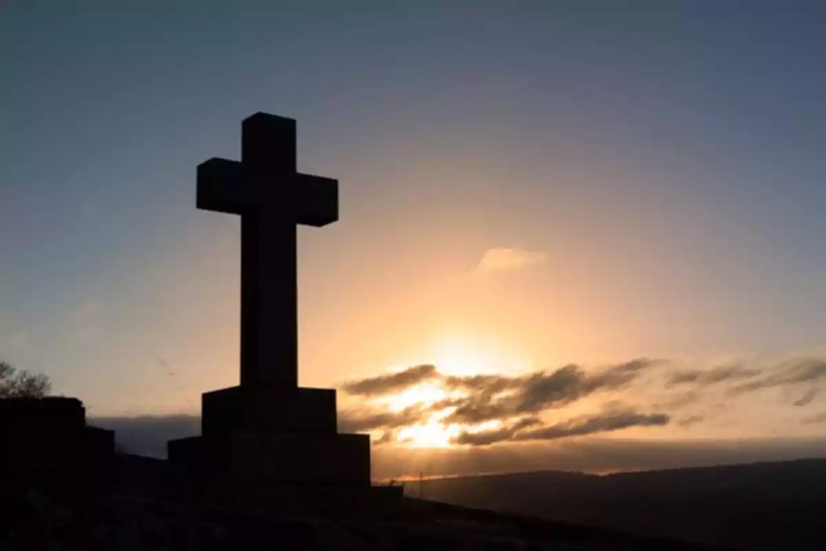 Creu en un turó al capvespre amb el cel il·luminat pel sol.