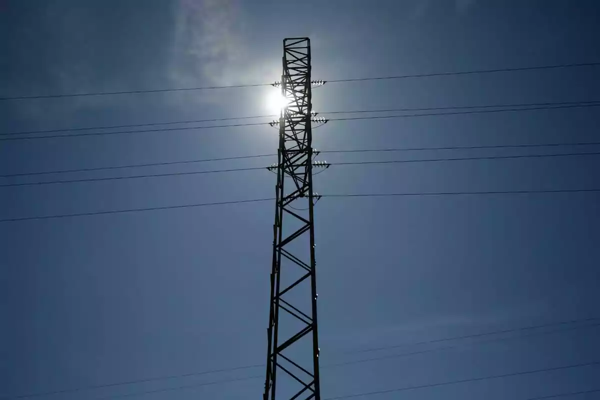 Torre d'electricitat amb cables i el sol brillant darrere en un cel clar. Torre d'electricitat amb cables i el sol brillant darrere en un cel clar.