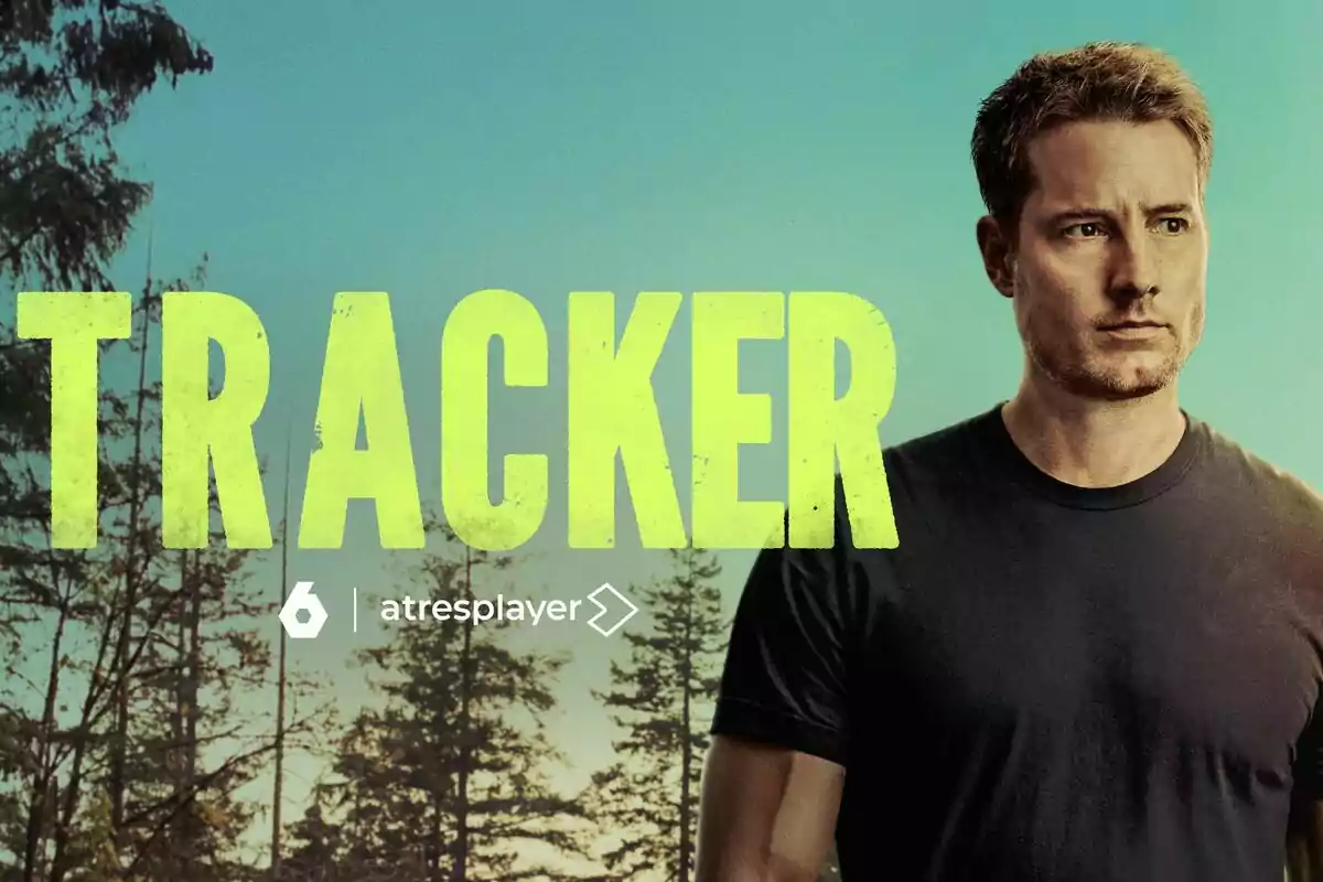 Justin Hartley de cabell curt i samarreta fosca dret al costat del títol Tracker en lletres grans grogues amb un fons d’arbres i cel blau