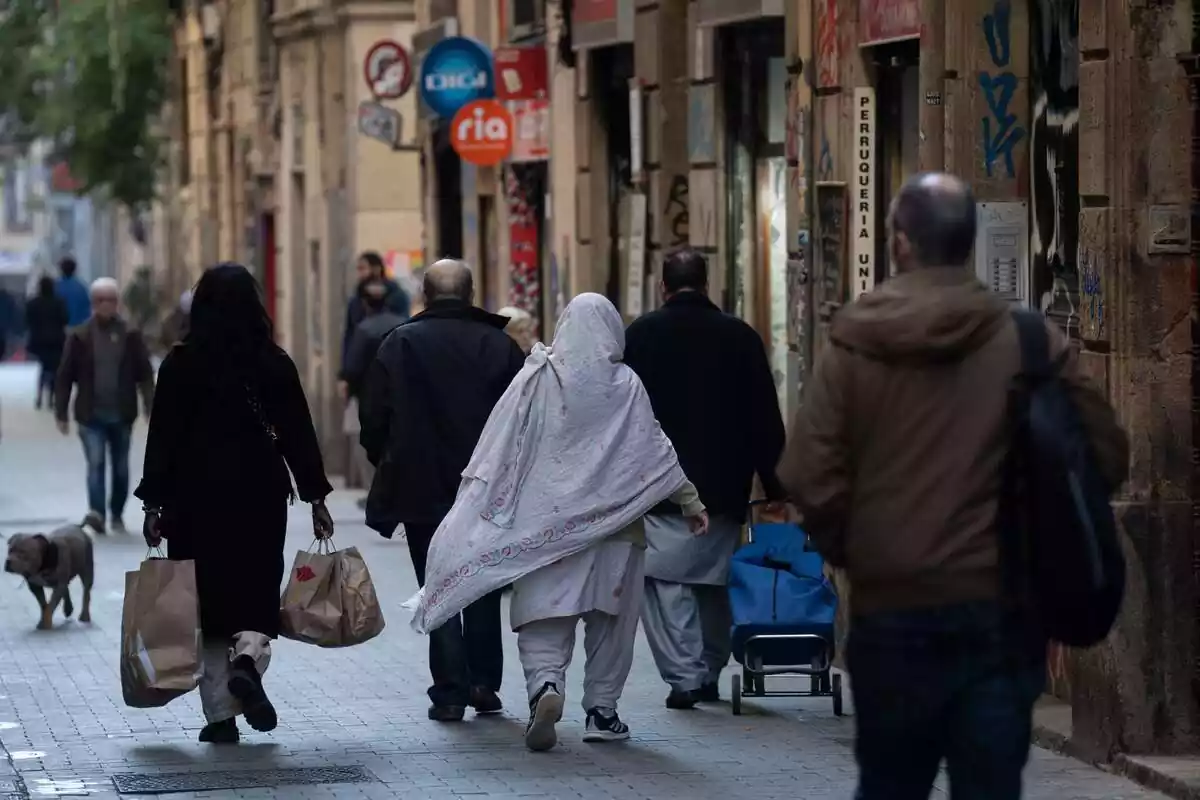 Transeünts immigrants en un cèntric carrer de Barcelona caminant d'esquena a la cambra