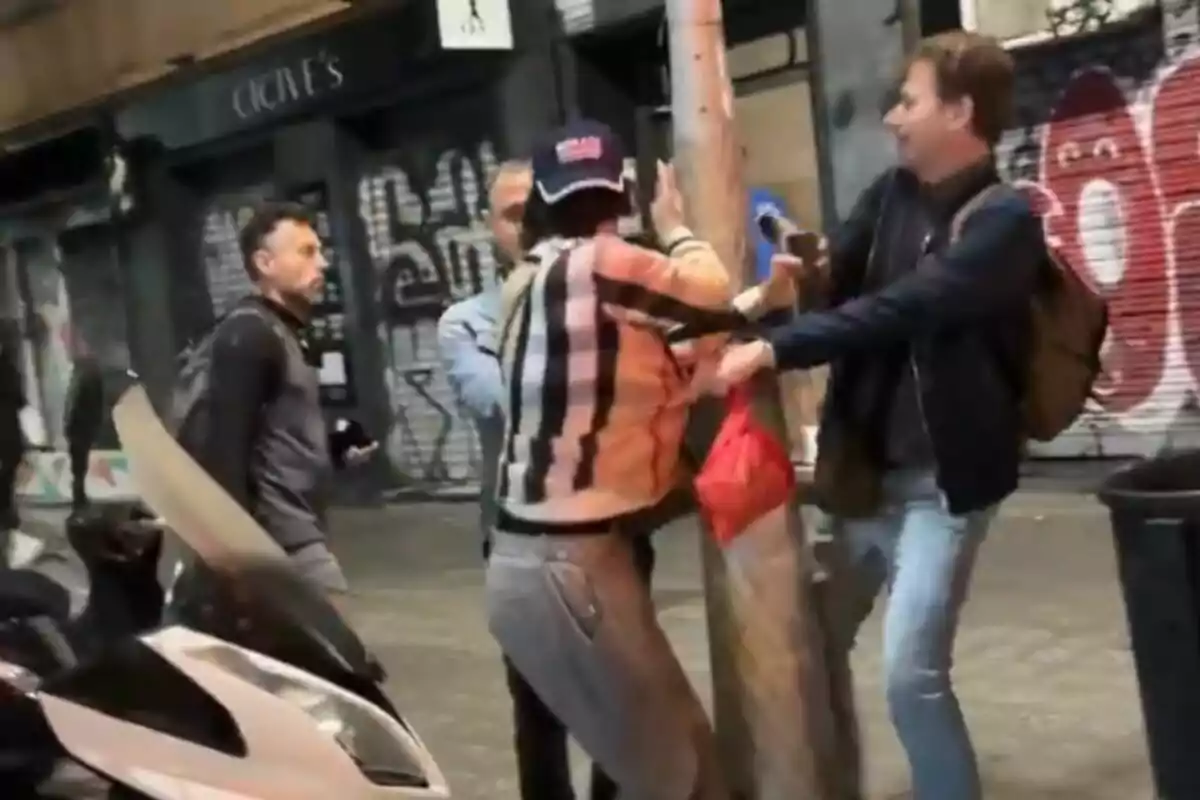 Un grup de persones interactua en un carrer amb grafits i una motocicleta estacionada a prop.