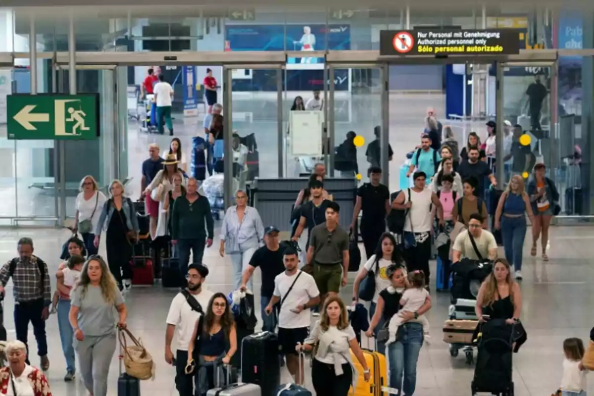 Persones caminant amb maletes a un aeroport, amb un rètol de sortida d'emergència a l'esquerra i un rètol de "Només personal autoritzat" a dalt.