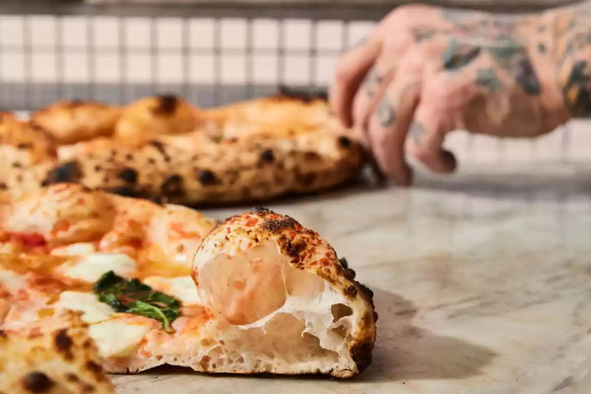 A pizza with a crispy crust and a tattooed hand in the background.