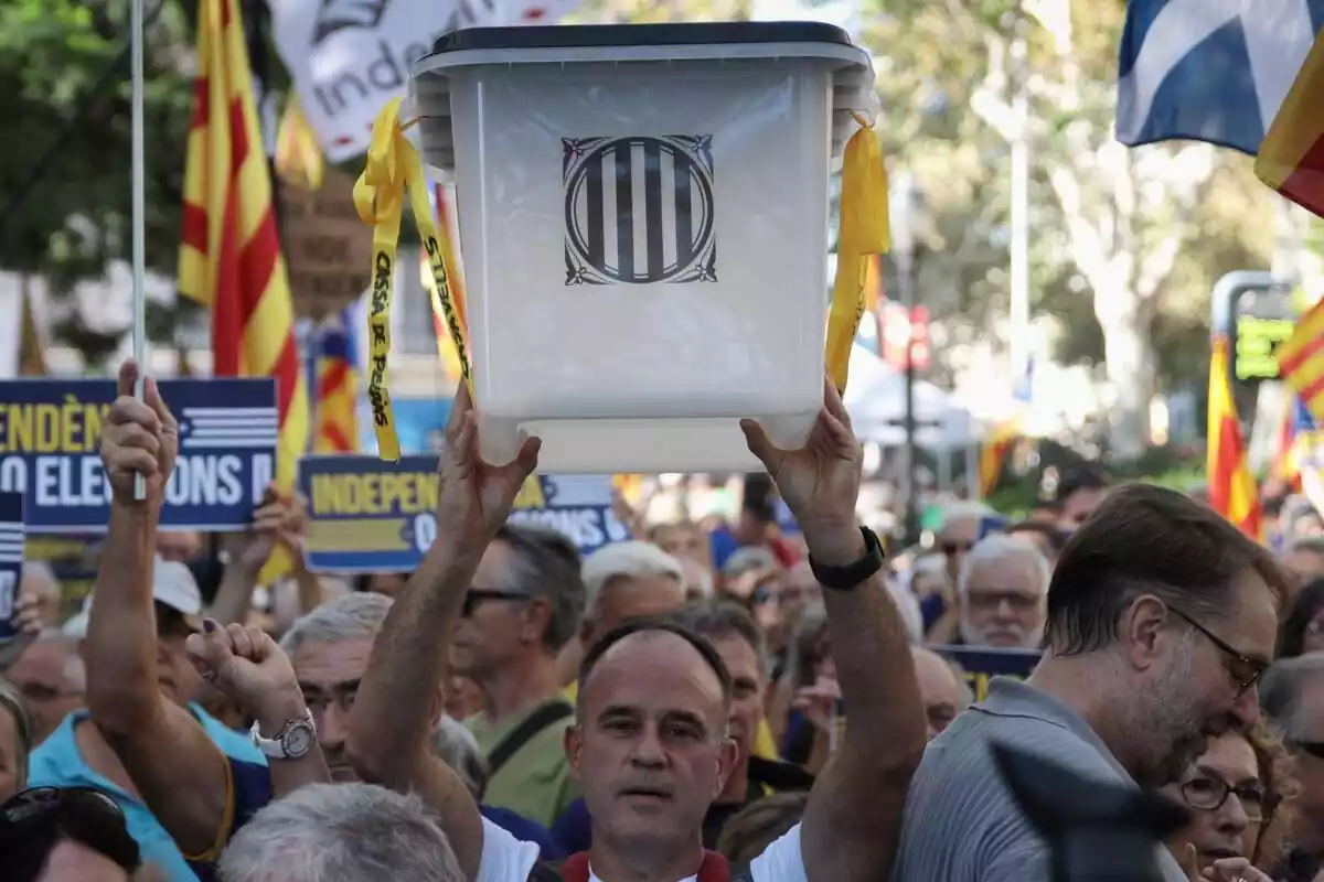 Un home calb subjecta i aixeca amb les dues mans una urna de les que es van fer servir per al referèndum de l'1 d'octubre a Catalunya. Ho fa enmig d'una manifestació, envoltat de desenes de persones