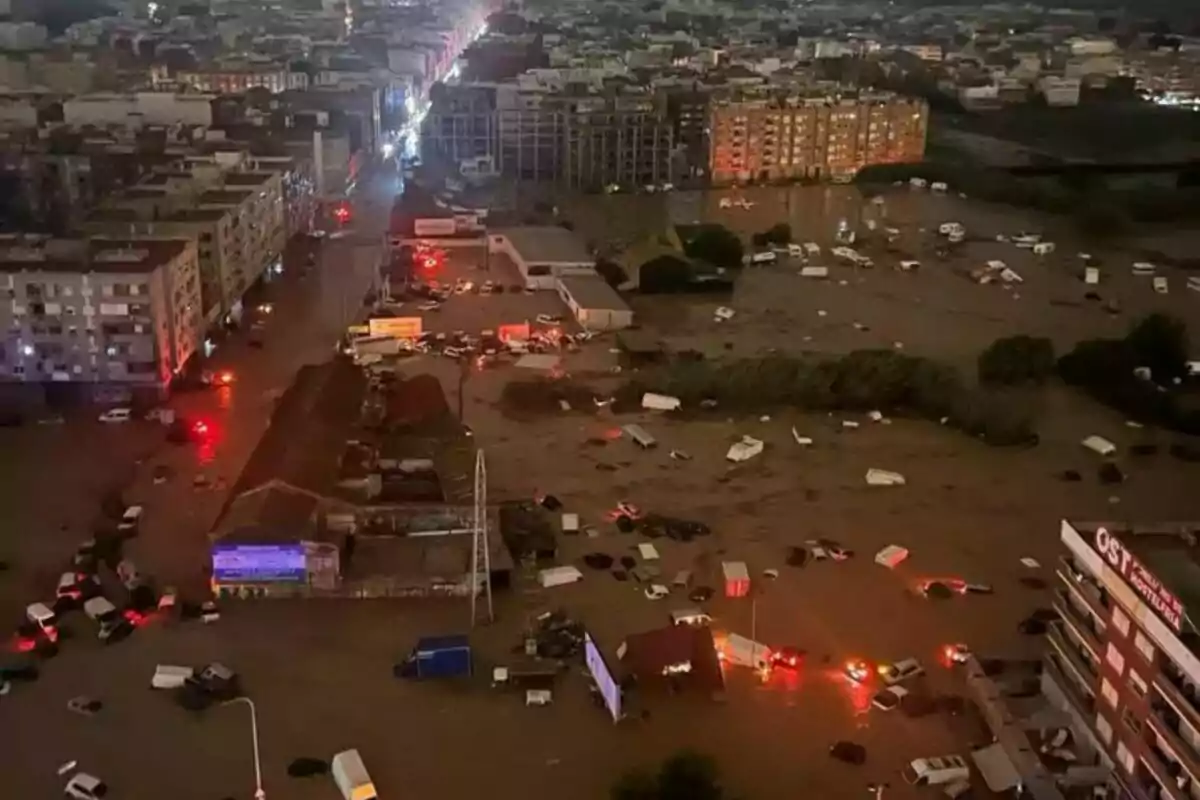 Vista aèria d?una ciutat inundada durant la nit amb carrers coberts d?aigua i vehicles submergits, llums d?emergència reflectits al?aigua.