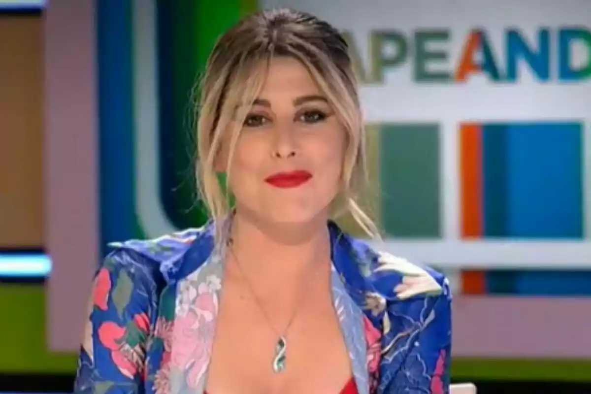 Valeria Ros amb cabell ros i llavis vermells, usant una jaqueta acolorida i un collaret, en un set de televisió amb un fons colorit a Zapeando.