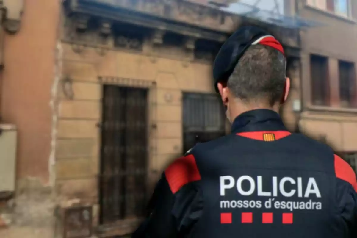 Un agent de policia d'esquena amb uniforme dels Mossos d'Esquadra davant d'un edifici antic.