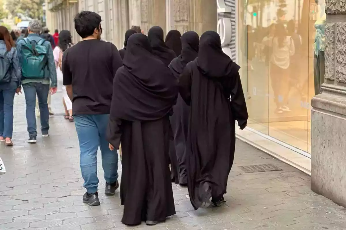 Diverses dones vestides amb niqab caminant pels carrers de Catalunya amb un home al costat