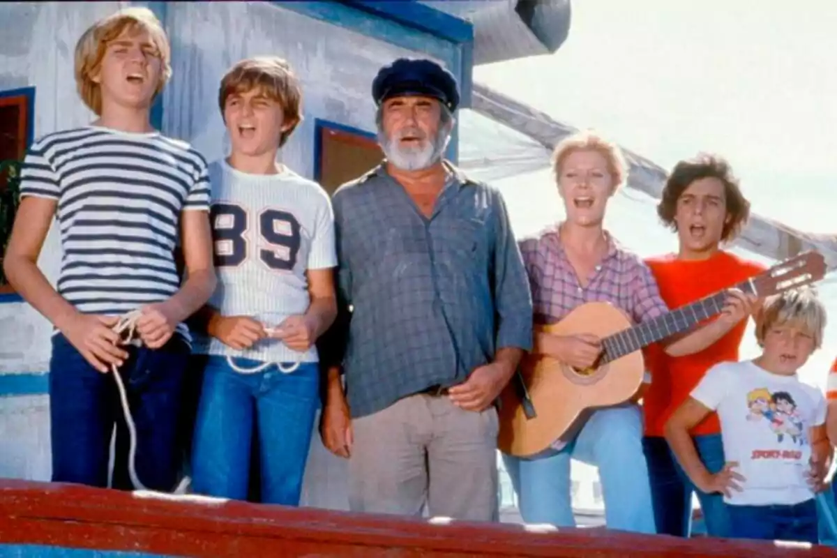 Protagonistas de Verano Azul, serie de RTVE, de pie en un barco, una de ellas tocando una guitarra.