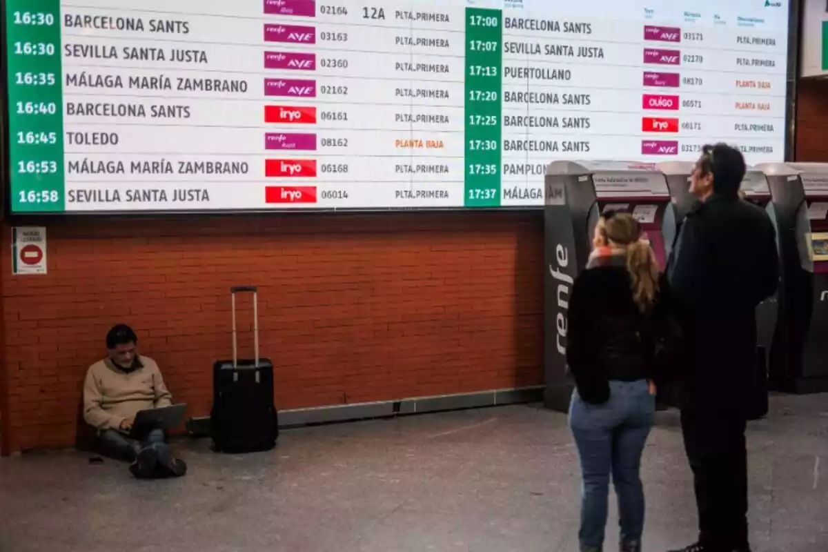 Diversos viatgers davant una pantalla anunciant les sortides i arribades de tren