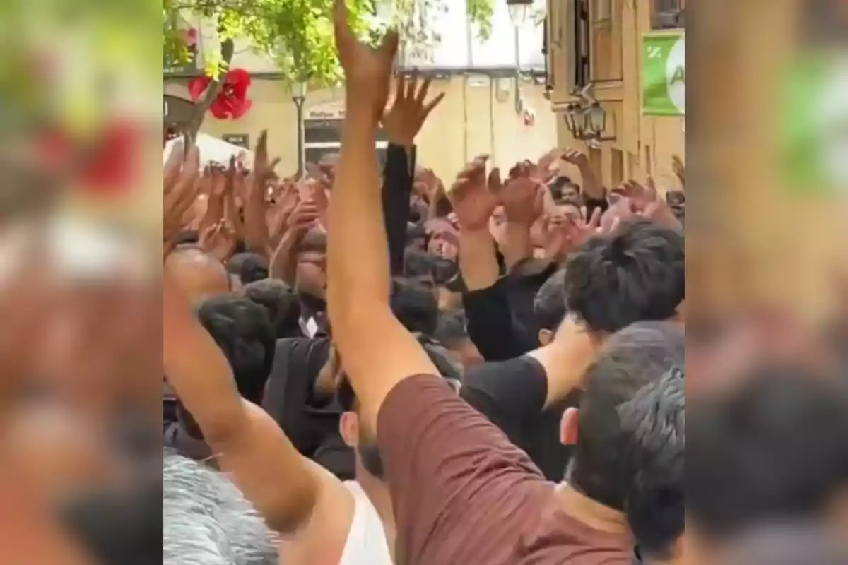 Una multitud de persones amb els braços aixecats a un carrer, envoltada d'edificis i arbres.