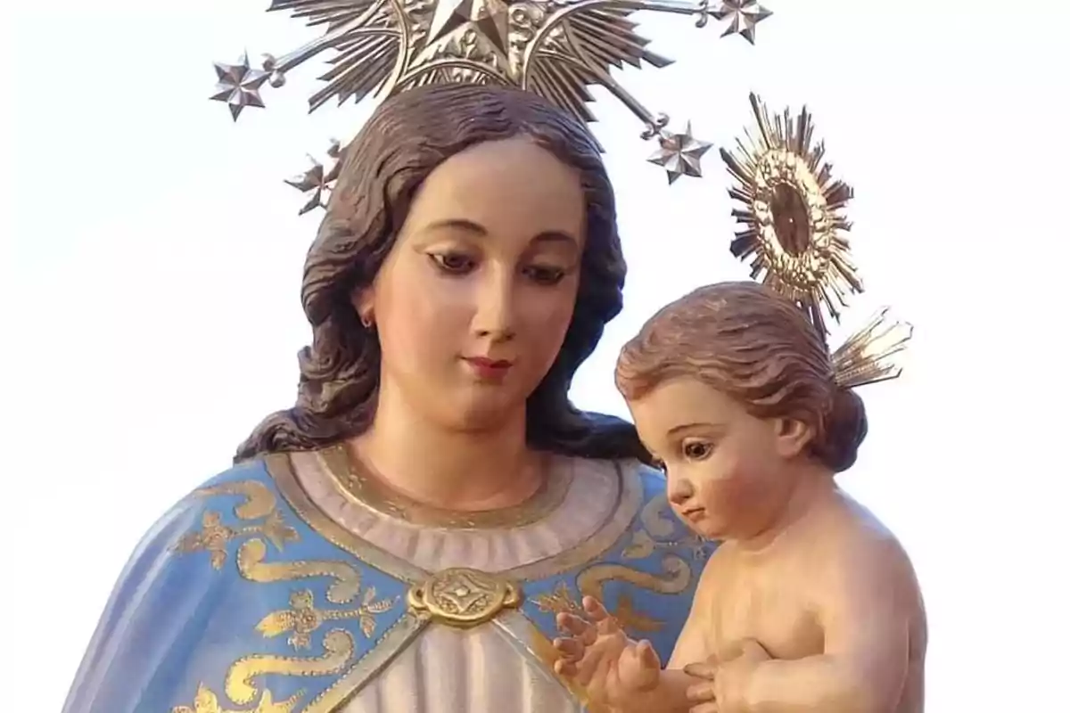 Una estatua religiosa de una mujer con un niño en brazos adornada con detalles dorados y una corona de estrellas.