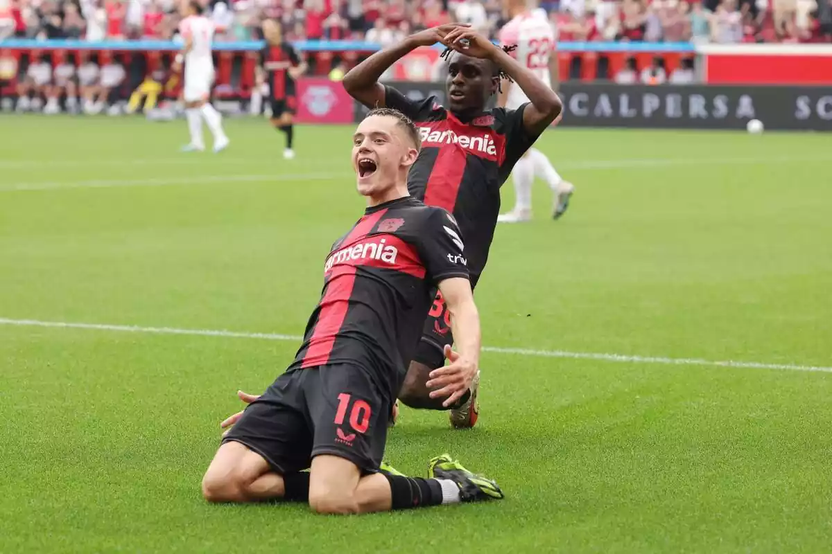 Florian Wirtz kneels on the grass to celebrate a goal