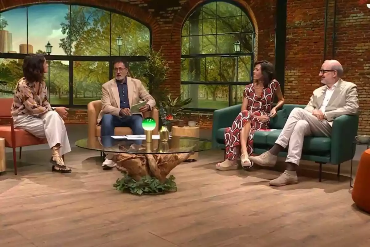 Xavier Grasset amb Antoni Bassas, Alba Alfageme i Maria Juan assegudes en un set de televisió amb una taula de centre de vidre i un fons que simula un parc a La Selva.