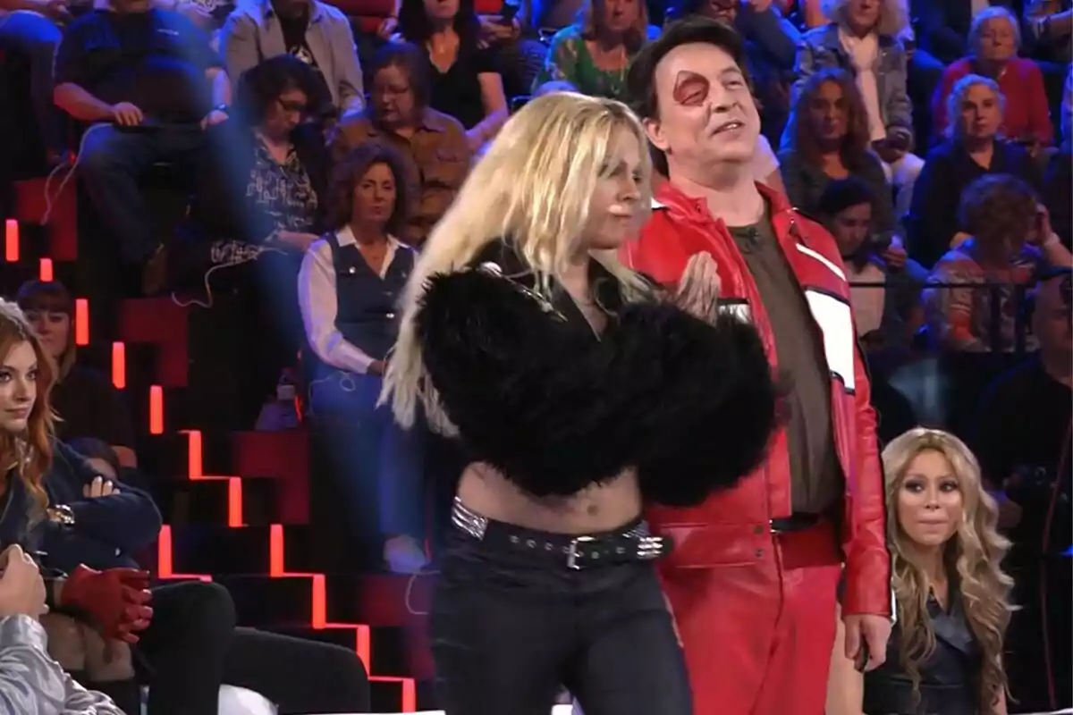 Un grup de persones està assegut en un estudi de televisió, mentre dos individus en primer pla, Goyo Jiménez amb jaqueta vermella i Yenesi amb jaqueta negra de pelfa, semblen estar participant a Tu Cara Me Suena. Un grup de persones està assegut en un estudi de televisió, mentre dos individus en primer pla, Goyo Jiménez amb jaqueta vermella i Yenesi amb jaqueta negra de pelfa, semblen estar participant a Tu Cara Me Suena.