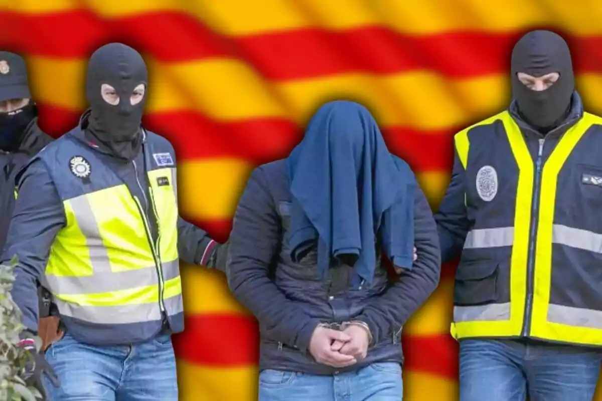 Policies emmascarats escorten un detingut amb el cap cobert davant d'una bandera de Catalunya.