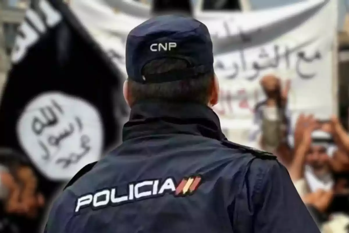 Un agent de policia d?esquena amb un grup de persones i pancartes al fons.