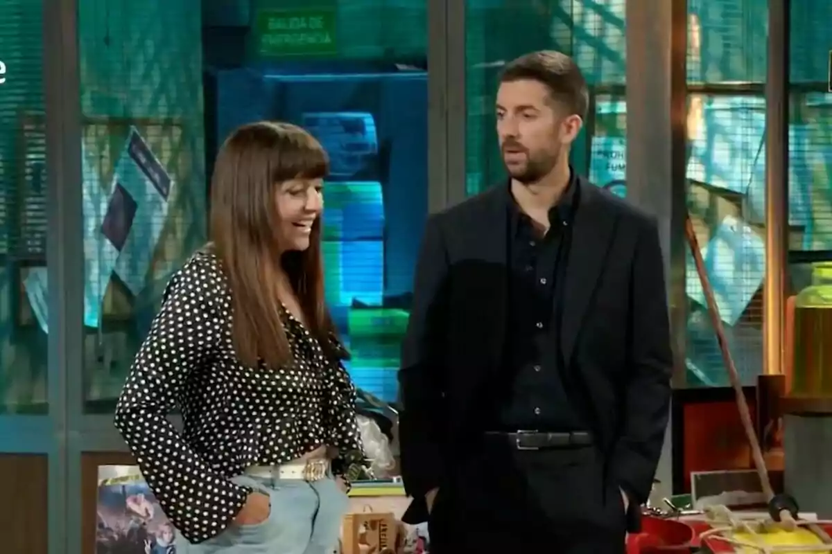 Yolanda Ramos i David Broncano conversen a 'La Revuelta' amb un fons d'objectes i rètols, una dona somriu mentre un home l'observa.
