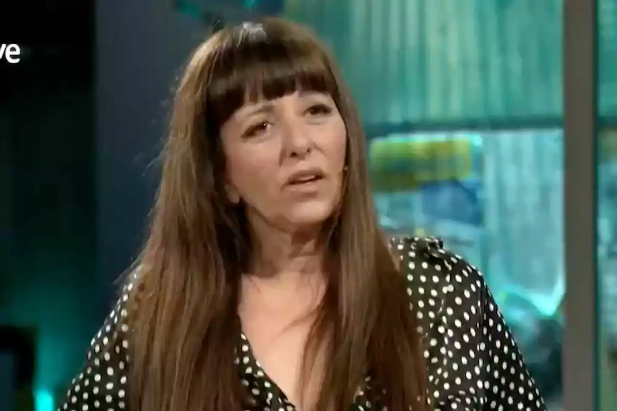 Yolanda Ramos amb cabell llarg i llis amb serrell, portant una brusa negra amb topos blancs, a 'La Revuelta' amb fons desenfocat.